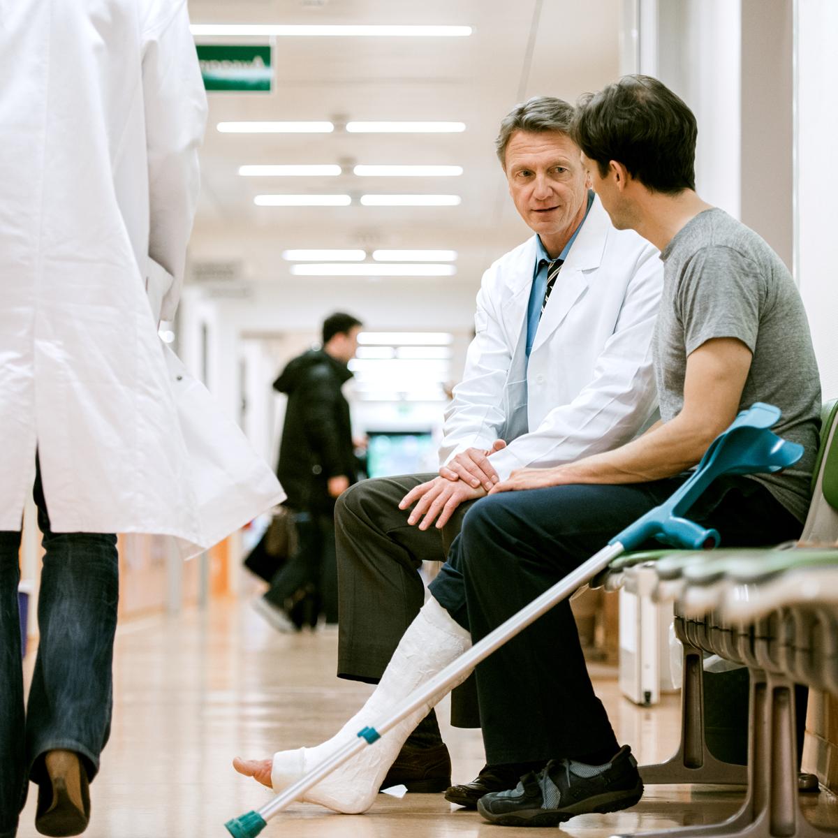 Man with crutches talking to doctor in hospital hallway.